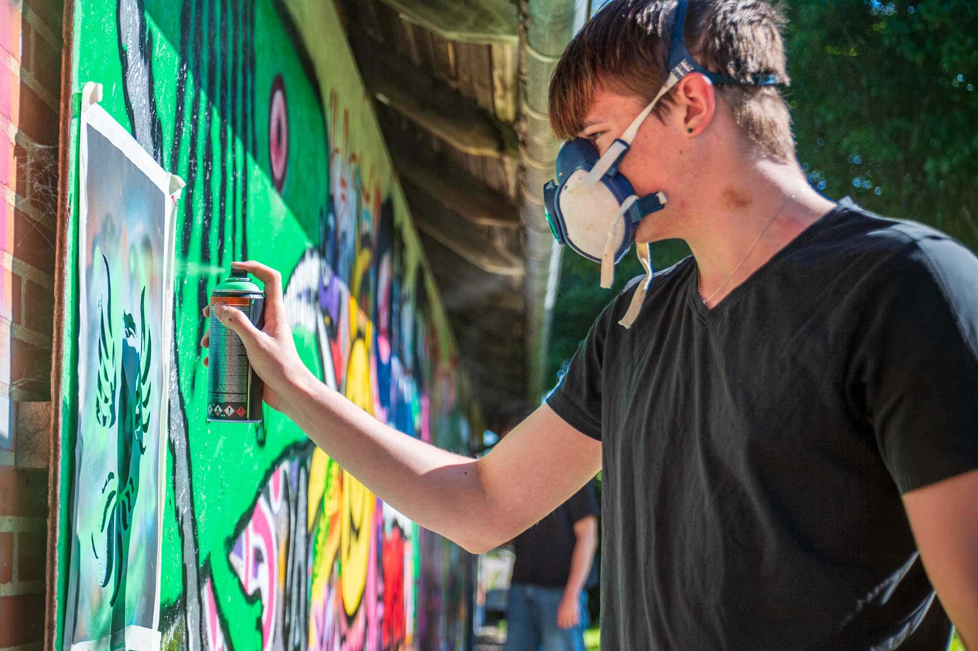 Elev laver graffiti med spraymaling og stencil på ArtXpress på Husby Efterskole