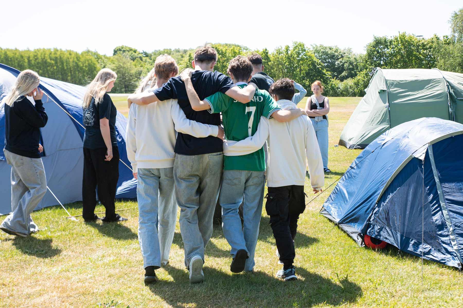 Elever går med armene om hinanden mellem telte på Husby Efterskole.