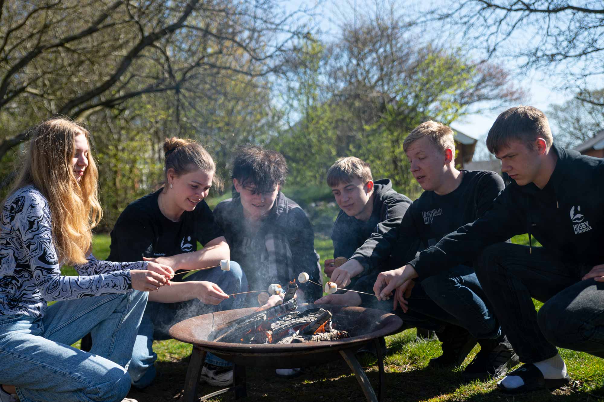 Elever hygger omkring bål under outdooraktivitet på Husby Efterskole